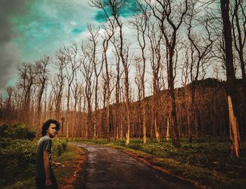 Man standing on road by bare trees in forest