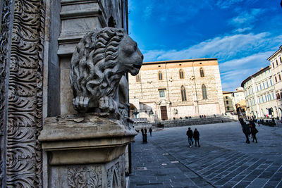 Statue by historic building in city against sky