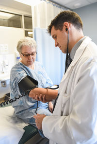 Doctor taking blood pressure of an older patient in clinical setting.