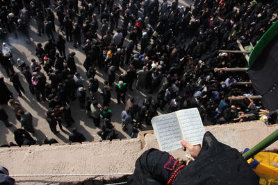 High angle view of person reading koran against crowd of people