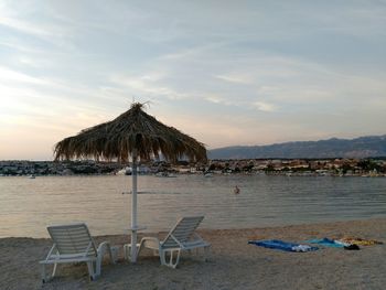 Chairs at beach against sky during sunset