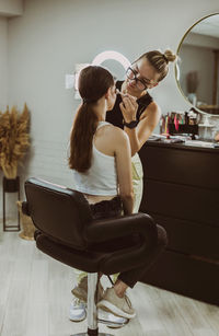 A young makeup artist applies eye shadow to a girl s eyelids with a brush.