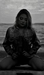 Young woman sitting on shore against sea