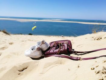 Shoes and bag on sand at beach against sky