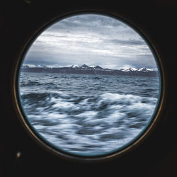 Scenic view of sea and snowcapped mountains against sky seen through window