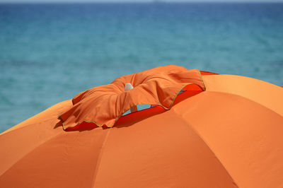 Close-up of orange umbrella on beach against sky