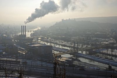 Factory emitting smoke by river in city