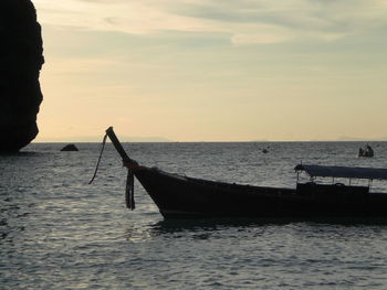 Silhouette longtail boat on sea during sunset