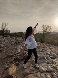Rear view of woman standing on rock against sky