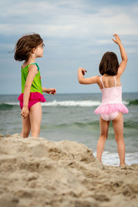 Sisters on rock at beach against sky