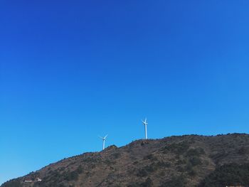 Low angle view of windmill on mountain against clear blue sky
