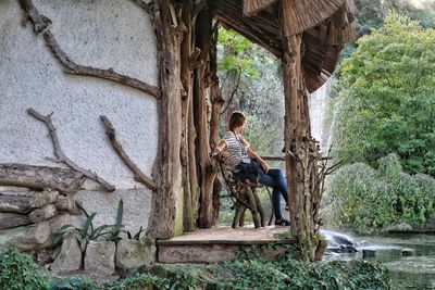 Side view of man sitting by plants against trees