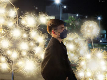 Portrait of young man standing by christmas tree at night