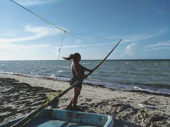 Woman standing by boat at shore of beach against sky