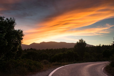 Road by silhouette trees against sky during sunset