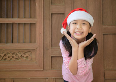Portrait of smiling girl wearing santa hat standing by window