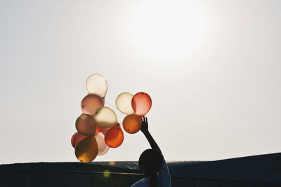 Rear view of woman holding balloons against clear sky on sunny day