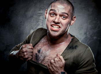 Portrait of muscular build man tearing t-shirt against gray background