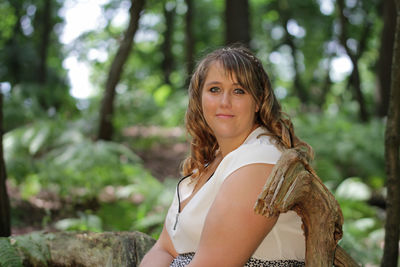 Portrait of young woman sitting on log in forest