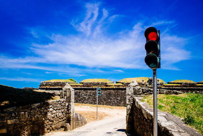 Illuminated red light by footpath against blue sky