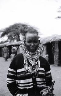 Portrait of woman wearing necklaces while standing against huts