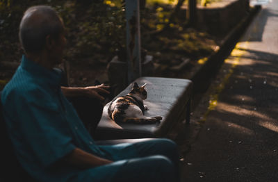 Man sitting on bench with cat outdoors