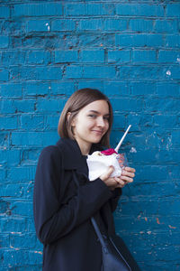 Portrait of young woman having ice cream by blue wall