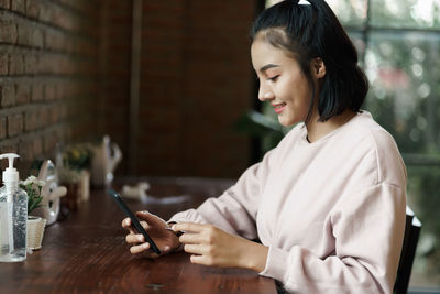 Young woman using smart phone on table at window