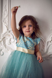 Child girl in a long menthol birch dress stands against the wall