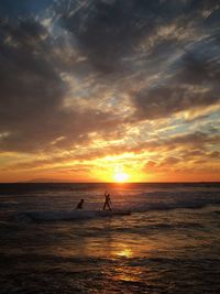 Scenic view of people swimming in sea and dramatic sky during sunset