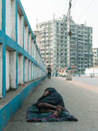 Man sleeping on street against buildings in city