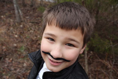 Portrait of cute boy with artificial mustache while standing outdoors