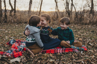 Three siblings sitting on red plaid blanket laughing