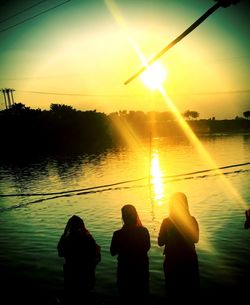 Rear view of silhouette people by lake against sky during sunset