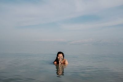 Portrait of young woman swimming in sea against cloudy sky