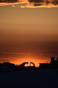 Silhouette city against dramatic sky during sunset