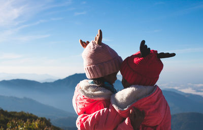 Siblings with arm around against sky