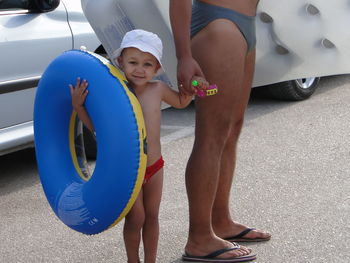 Portrait of boy holding inflatable ring while standing with father on road