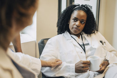 Serious female doctor with coffee cup looking at colleague during break in hospital