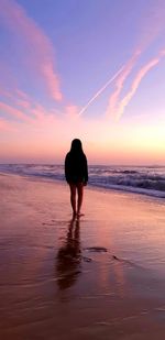 Rear view of silhouette standing on beach against sky during sunset