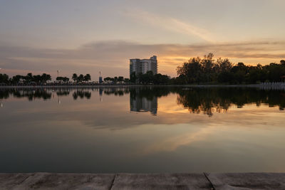 Scenic view of lake by silhouette buildings against sky during sunset