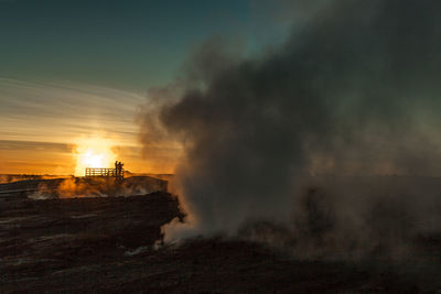 Smoke emitting from silhouette landscape against sky during sunset