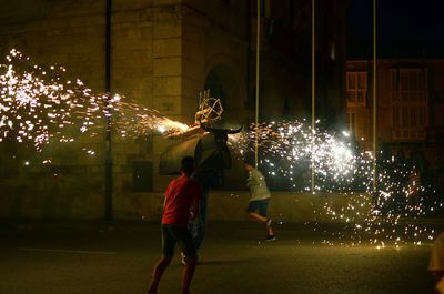 Rear view of people watching firework display at night