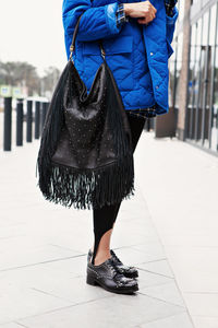 Close up black leather hand bag with fringe, boots with iron studs, vibrant puffer jacket