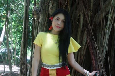 Portrait of young woman standing by tree in forest