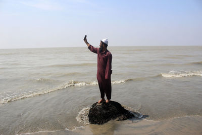 Man taking selfie while standing on rock at beach