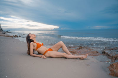 Young woman relaxing on beach against sky
