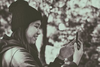 Smiling woman using mobile phone against tree