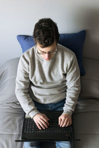 Young man using laptop while sitting on sofa at home