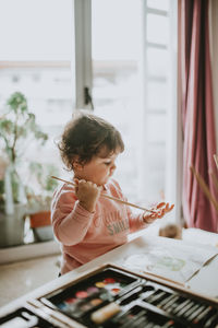 Girl painting while sitting on table at home